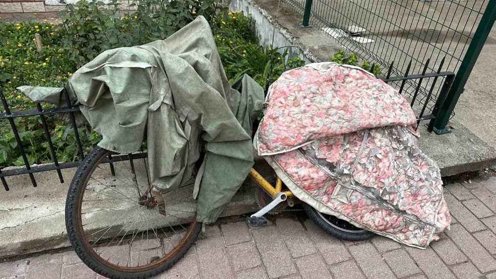 Bisikletini yağmurdan korumak için paltosuyla sardı
